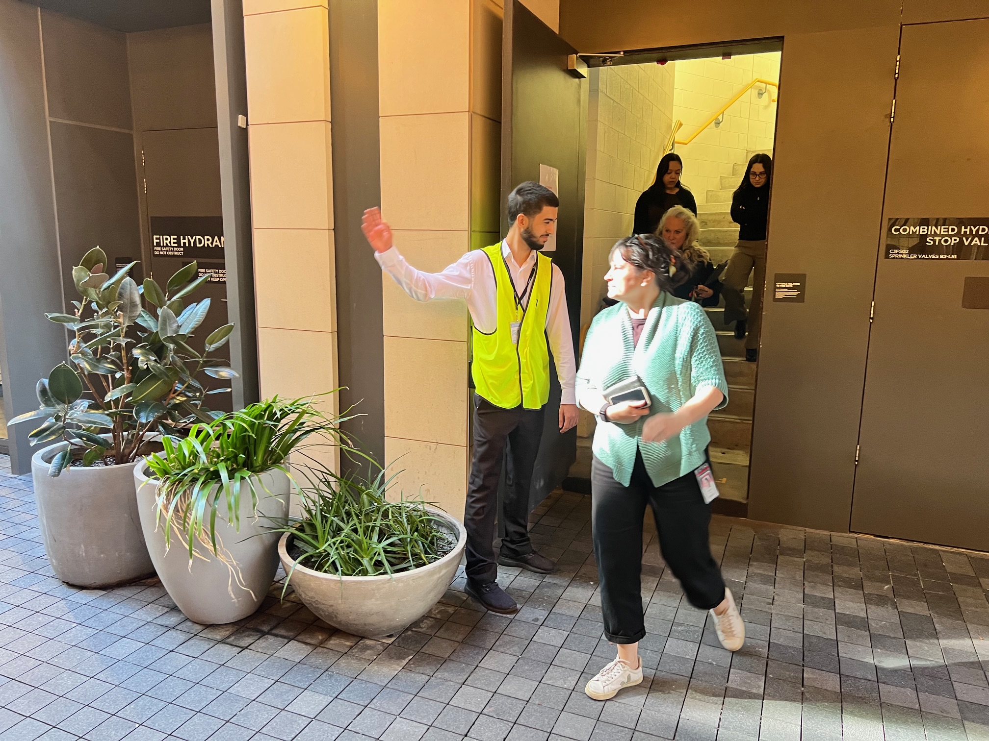 Warden in a hi-vis vest directing people out of a building stairwell exit
