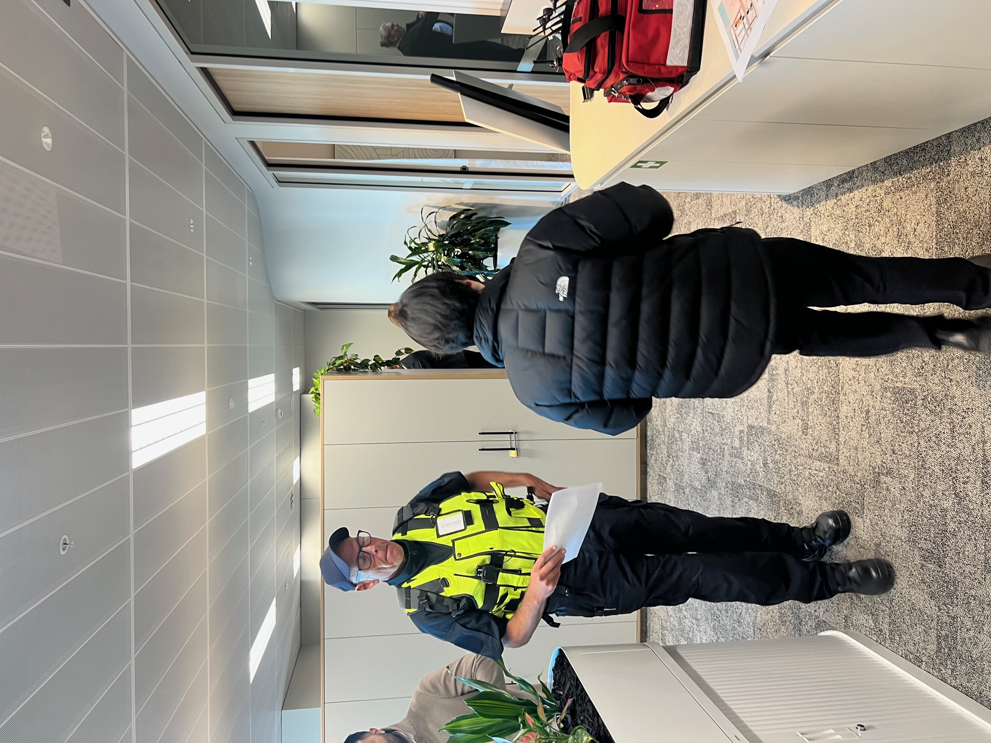 Security officer in hi-vis briefing a staff member in an office lobby